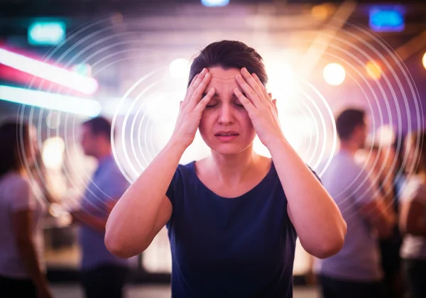 Person overwhelmed by sensory input in a noisy, bright social setting